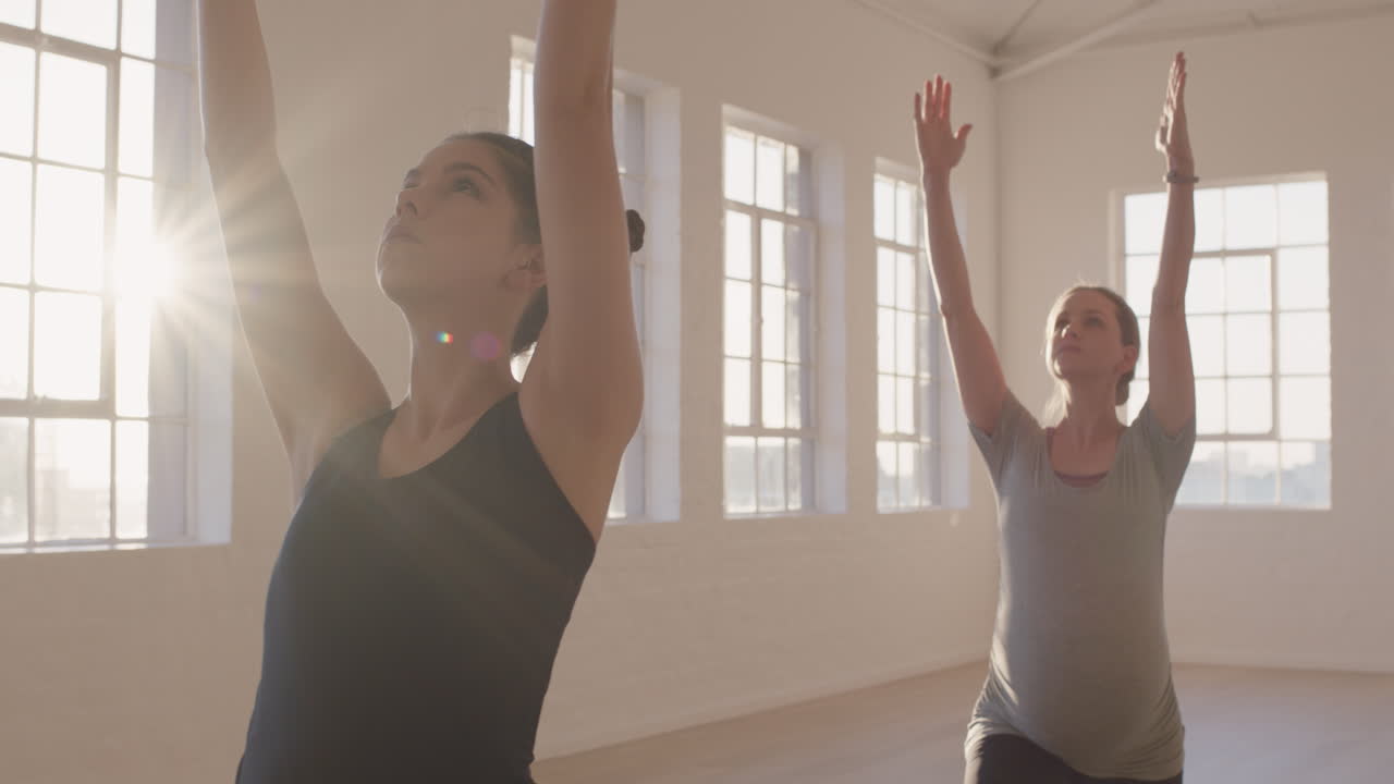 clase de yoga de mujeres embarazadas sanas practicando pose guerrera disfrutando de ejercicios físicos grupales con instructor en el estudio al amanecer