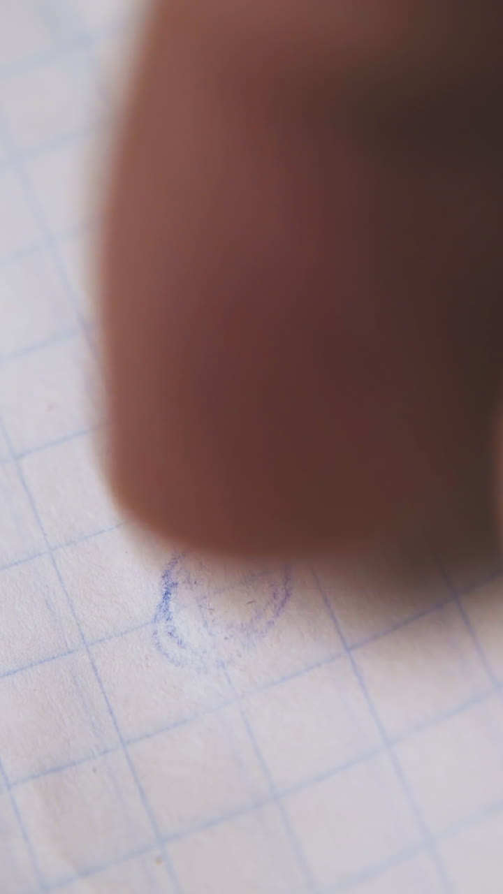 person hand erases funny picture drawn with pencil from checkered paper with rubber extreme close view