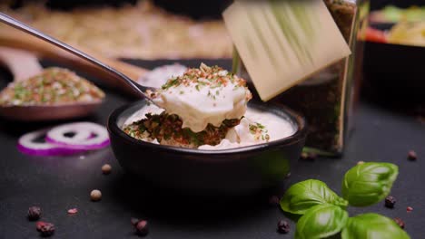 static shot of falling spices with basil, paprika, garlic and bell pepper in a bowl filled with delicious sour cream