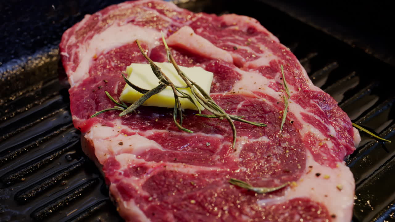 Burro che si scioglie su una bistecca condita che cuoce su una padella griglia calda con rosmarino
