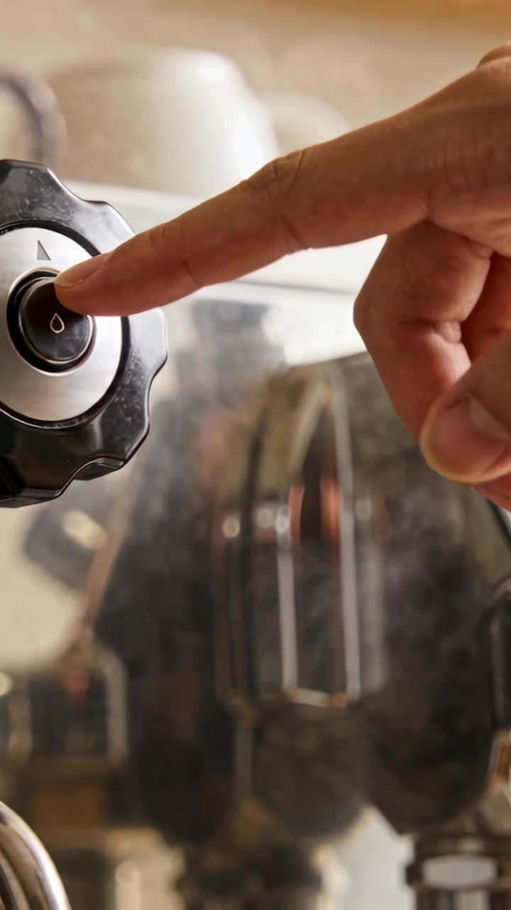 Video verticale: Mano destra che preme e aziona la manopola del caffè in cucina, avviando la produzione di vapore e caffè.