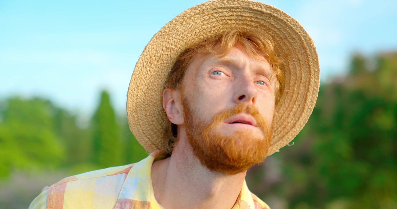 Thoughtful Red-Bearded Man in Straw Hat Looking Up Outdoors