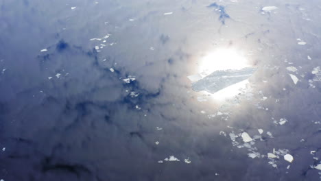 Drone-video-of-ice-rafts-or-floes-floating-in-water,-blue-sky-and-bright-sun-reflecting-from-the-surface-of-the-water