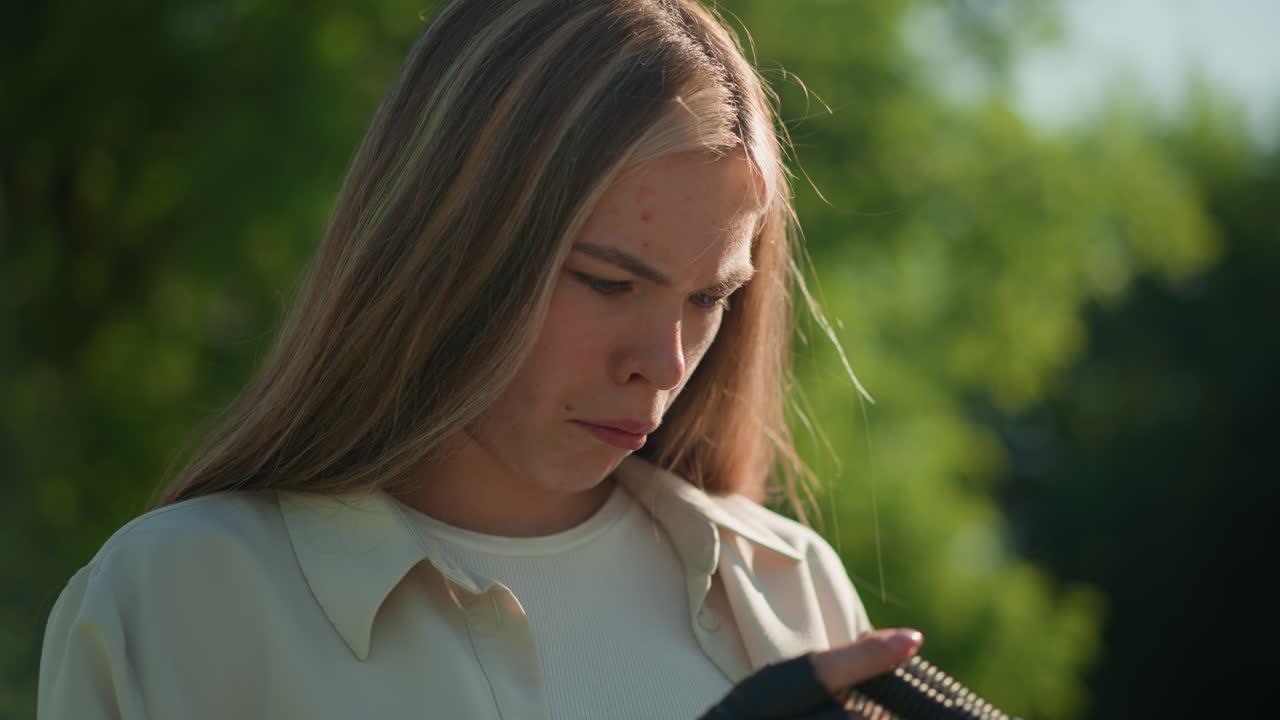 숙고한 표정을 가진 젊은 여성은 야외에서 초록색 공기 프를 조사하고, 울창한 초록색 가운데 서서, 장갑을 착용하고, 그녀는 장비에 집중하고 참여하는 것처럼 보입니다.