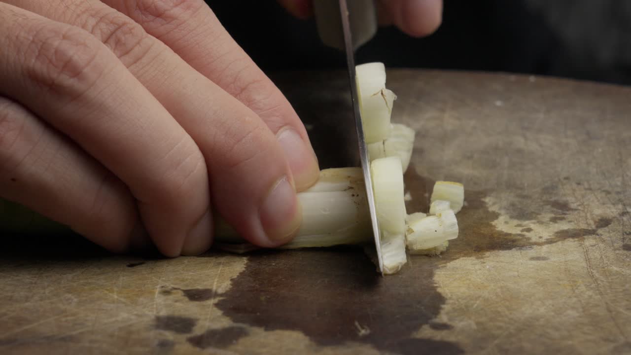 Primo piano, taglio di porro fresco con un coltello su un tagliere, scena di cucina.