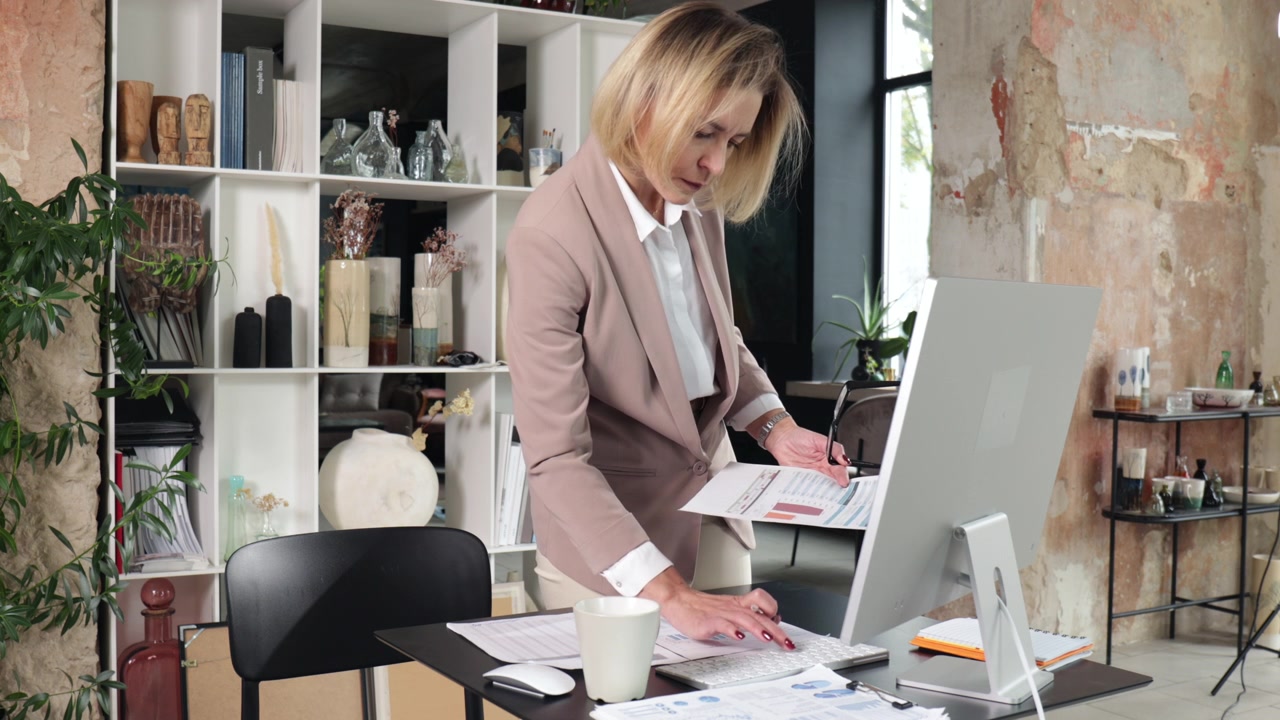 Empresária Focada Revisando Documentos e Digitanto no Computador de Mesa