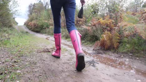 Close-up-of-female-dog-walker's-wellies,-walking-through-mud