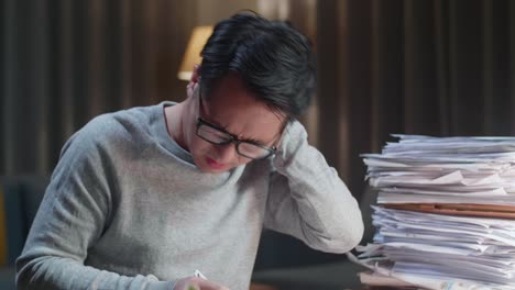 close up of asian man having neck pain while working hard with documents at home