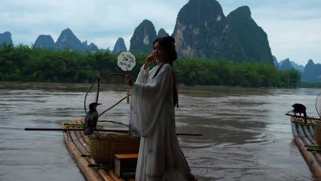 hanfu girl balances on a bamboo raft with round fan and cormorant during a photo session