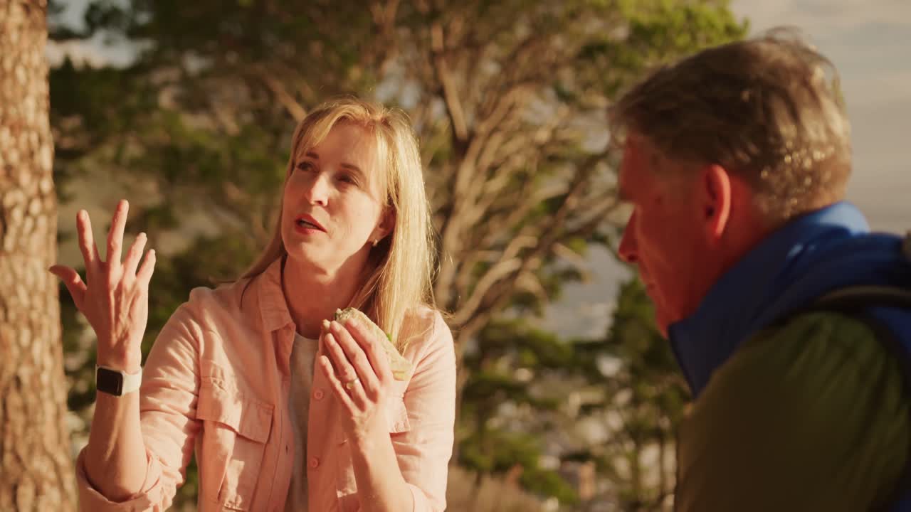 pareja de ancianos activos comiendo y sentados en un banco en el bosque