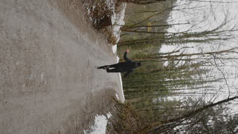 joven con cabello oscuro corto y chaqueta negra corriendo en un camino en el bosque en un día nublado