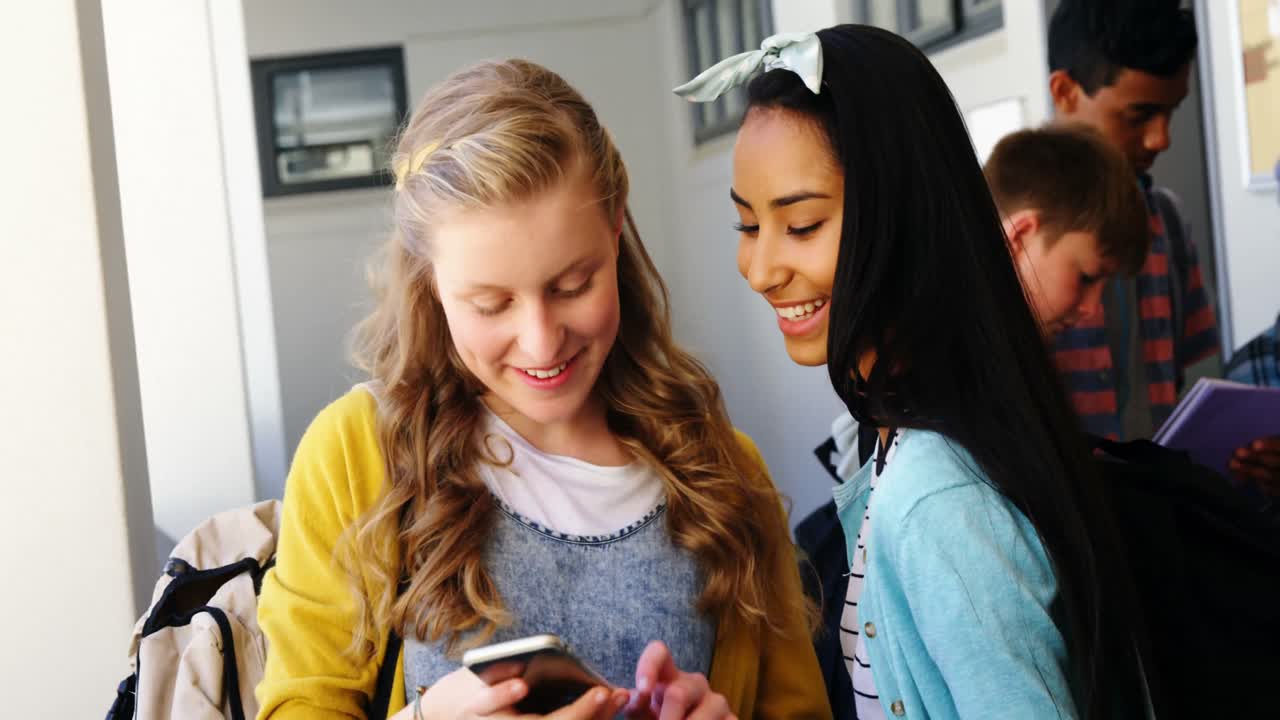 escolares sonrientes tomando selfies con teléfonos móviles en el pasillo