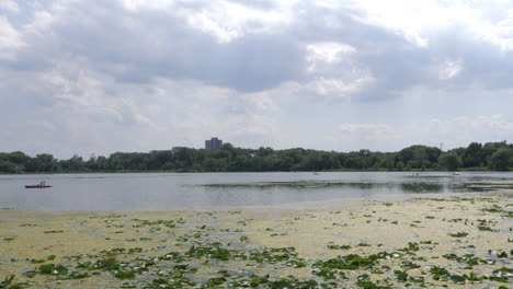 Städtischer-See-Mit-Seerosen-Und-Kleinen-Booten-In-Der-Ferne