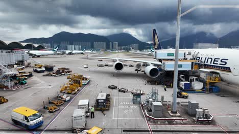 airplane being unloaded at hong kong international airport amid dramatic clouds. ground crews and vehicles are busy with logistics and handling, set against a mountainous backdrop.