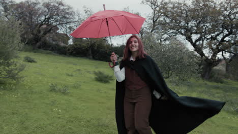 una mujer feliz gira en un prado durante la lluvia en invierno con un paraguas rojo