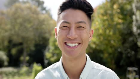 Portrait-of-happy-biracial-man-looking-at-camera-and-smiling-in-sunny-garden,-in-slow-motion