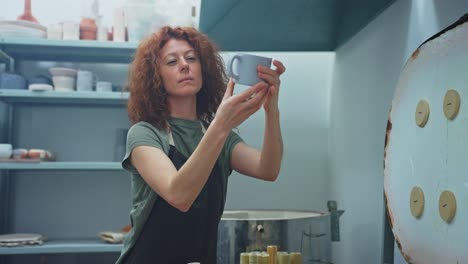 woman inspecting a handmade ceramic mug in her pottery studio