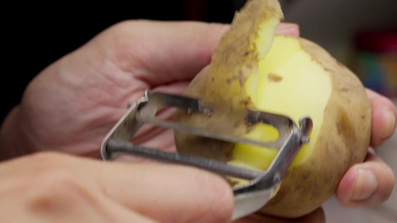 Scena dettagliata di preparazione del cibo con una patata appena sbucciata.