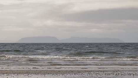 la isla escocesa de eigg vista desde una playa de la isla de skye con las olas rompiendo.