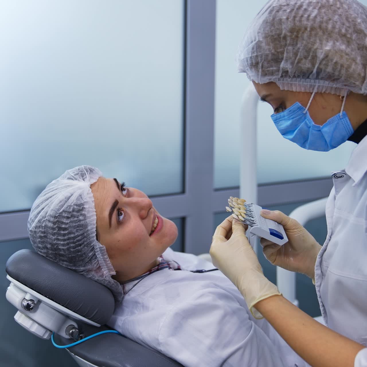 Two female students of dentistry department at practice. Future dentist chooses the best color species of teeth corresponding to the patient