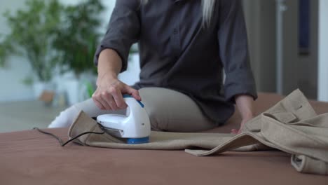 mujer utiliza una máquina para quitar pellets y bobinas de la ropa y la tela en pantalones negros. un dispositivo electrónico moderno para actualizar cosas viejas