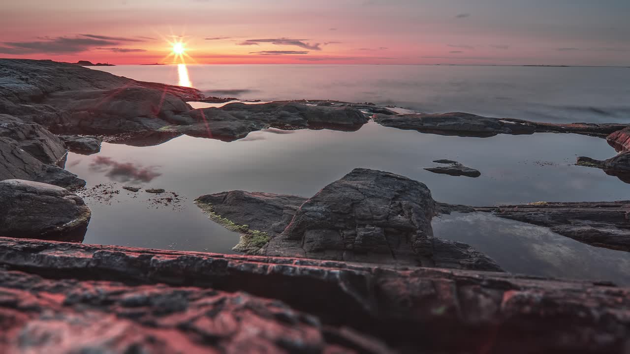 el sol rojo al atardecer y el cielo oscuro se reflejan en el mar tranquilo y las piscinas de marea poco profundas en la costa rocosa.