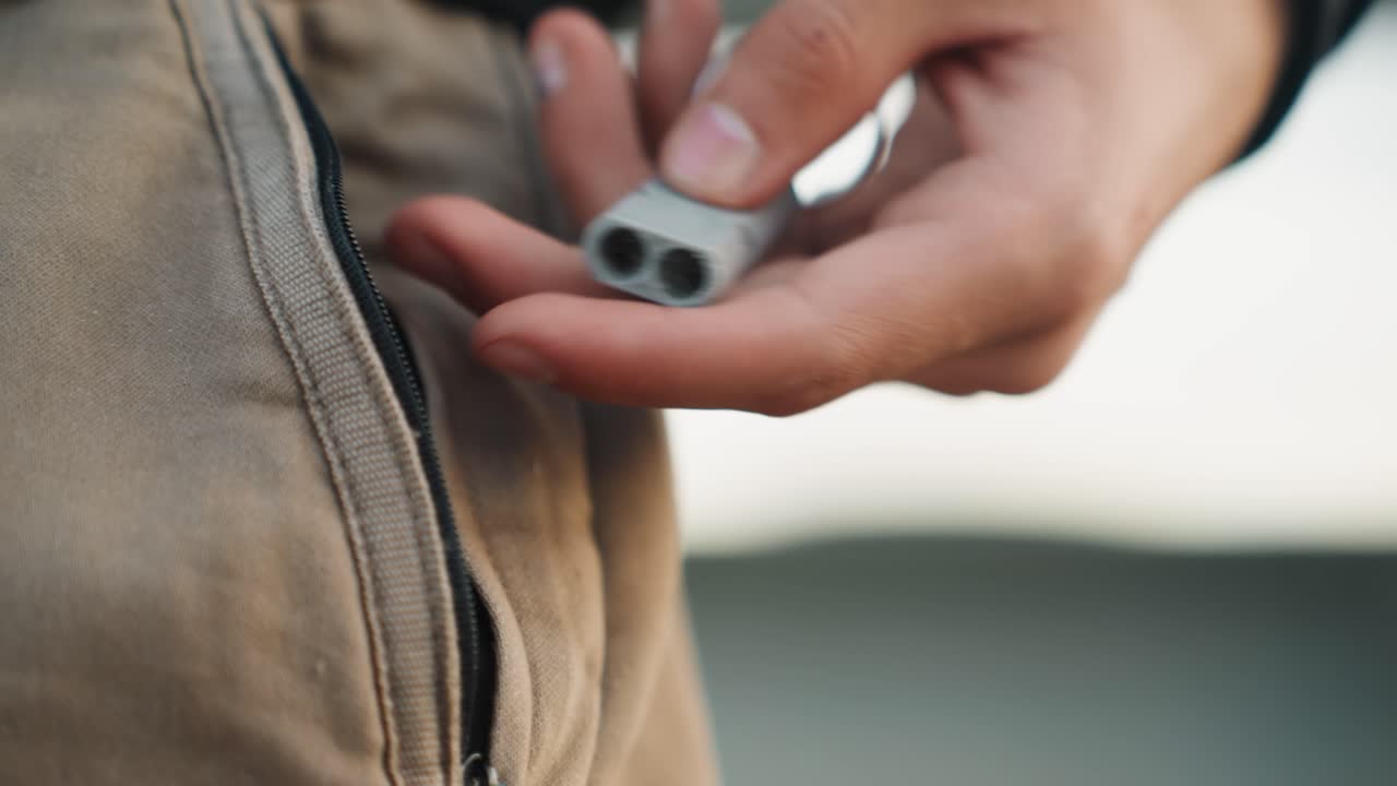 Tangan dengan perangkat abu-abu. Gambar fokus tangan memegang alat elektronik di pagi hari. Gambar makro yang menampilkan tangan memegang perangkat elektronik dengan latar belakang lingkungan komuter
