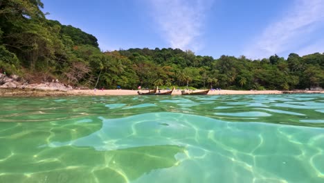 longtail boats float near a lush, tropical beach with clear turquoise waters under bright sunlight in phuket, thailand