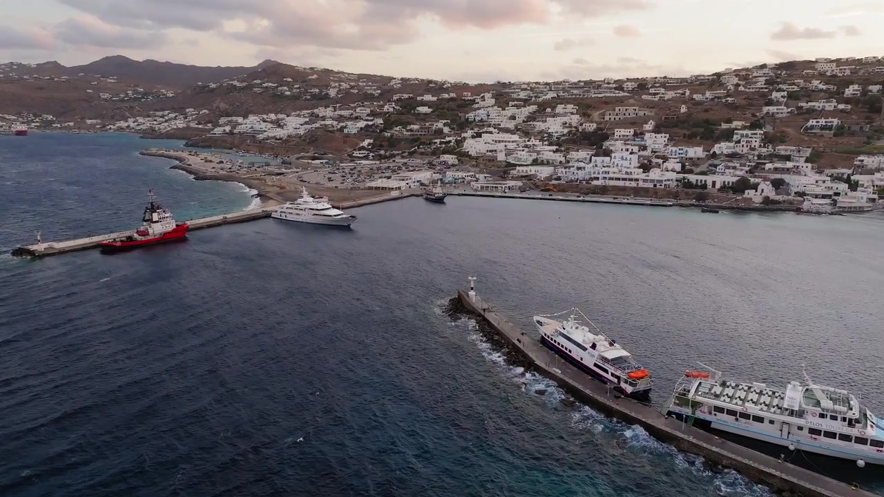 Panorama con drone sul vecchio porto di Mykonos all'alba. Barche ormeggiate, città imbiancata a calce, nuvole sparse. Luce dorata del mattino