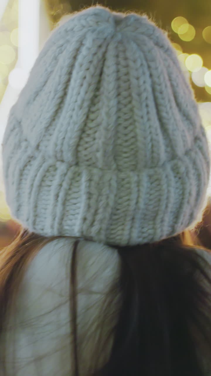 Close-up rear view of woman in warm winter outfit strolling through a beautifully illuminated city at night, star-shaped festive lights and blurred pedestrians