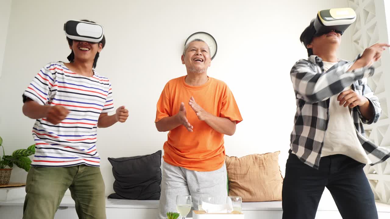 Happy Asian Father Cheering On His Sons Who Is playing Video Games Using VR Glasses At Home