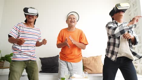 happy asian father cheering on his sons who is playing video games using vr glasses at home