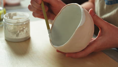 female hands brushing glaze onton clay mug at art studio. closeup shot