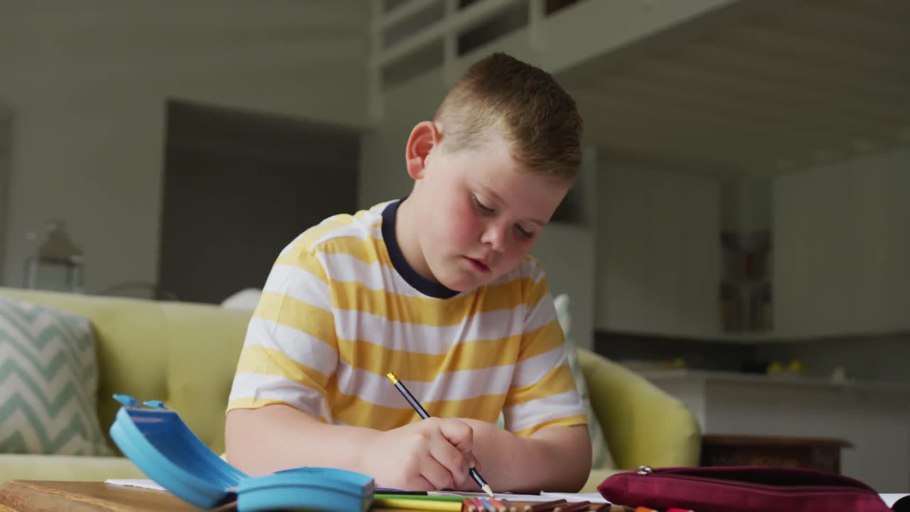 테이블에 앉아서 집에서 혼자 공부하는 백인 소년