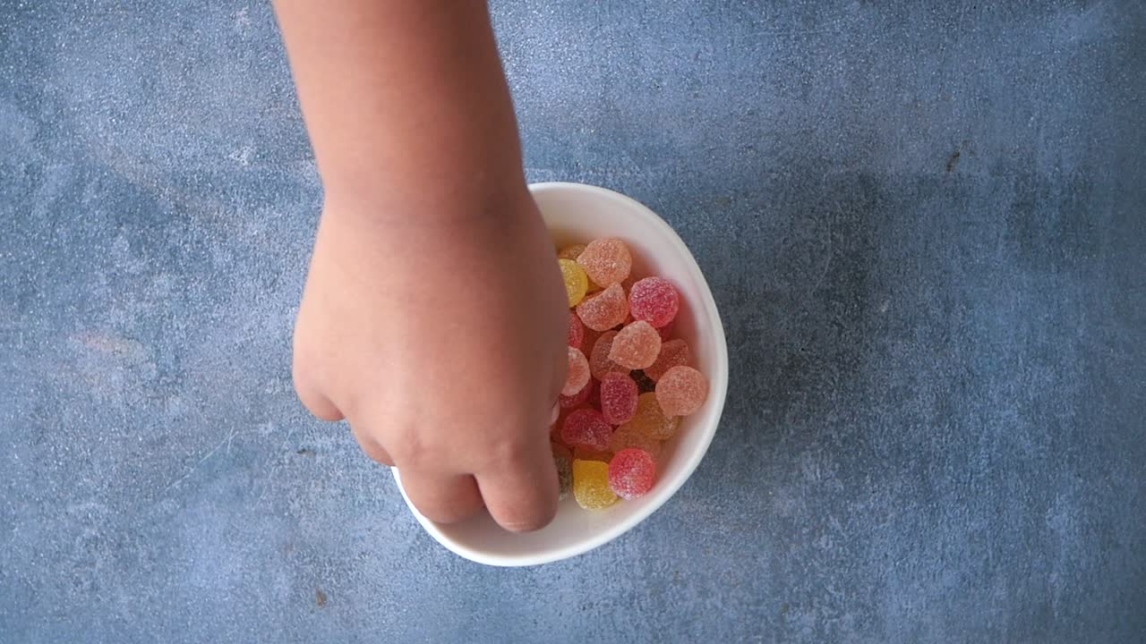 la mano de un niño alcanza un cuenco colorido de caramelos de goma