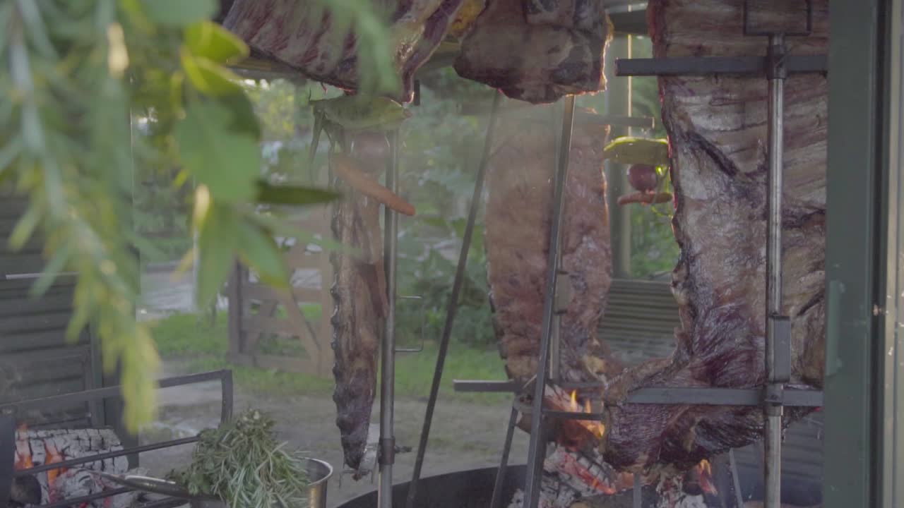 Slow motion handheld shot of raw meat asado being cooked and smoke passing by