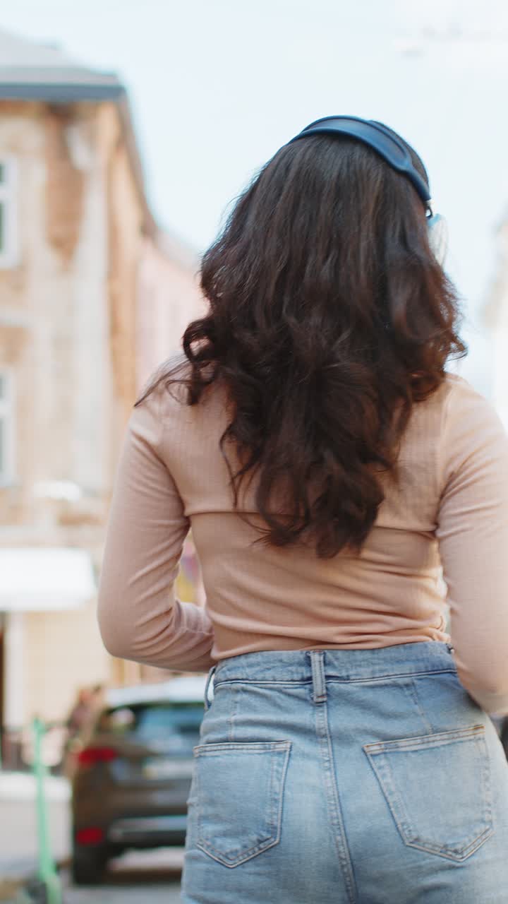 mujer india feliz con auriculares inalámbricos escuchando música en una aplicación de teléfono inteligente bailando en la calle de la ciudad