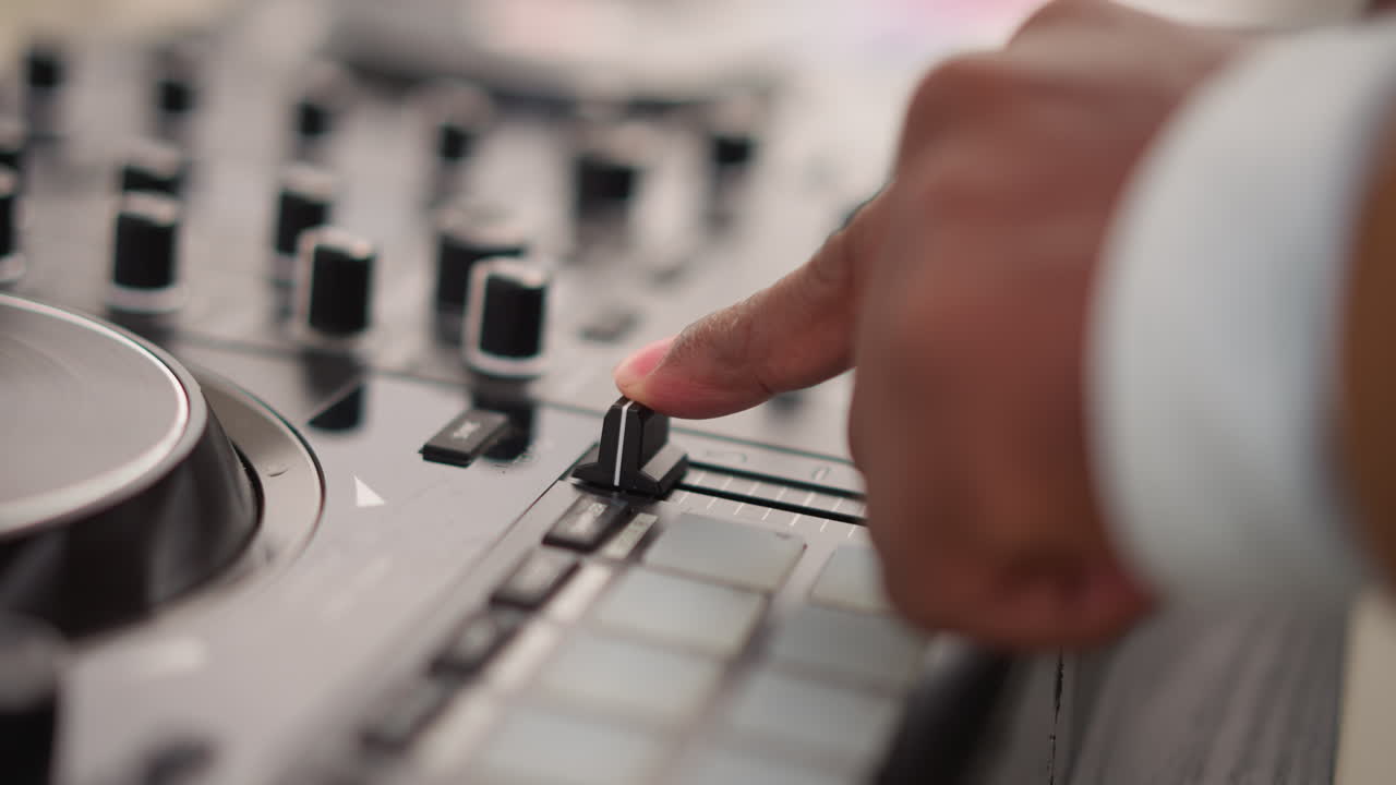 DJ negro con el dedo en el fader, primer plano de los controles deslizantes y pads de la mesa de mezclas, sesión de práctica concentrada con beat juggling táctil, técnicas de productor e ingeniero, poca profundidad de campo, movimiento concentrado