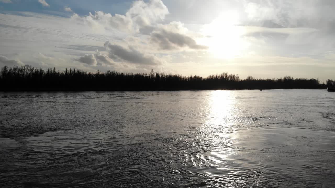 햇빛은 네덜란드 즈위인드레흐트 근처의 우데 마스 강에서 일몰 동안 조용한 호수를 통해 반사됩니다.