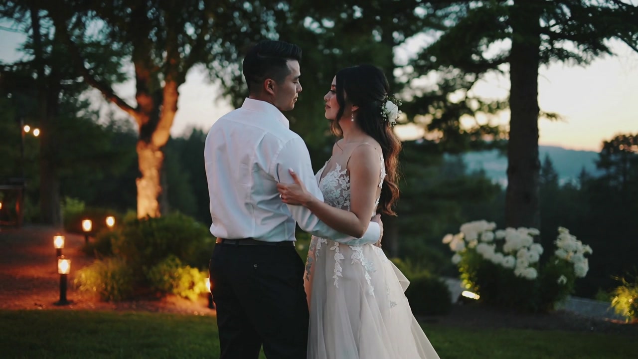 Dancing bride and groom swaying on lawn, dusk settling and celebrating wedding in gown and shirt