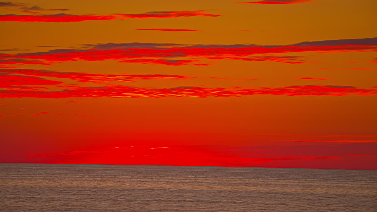 Time lapse of red colored clouds flying over ocean after spectacular sunset at horizon