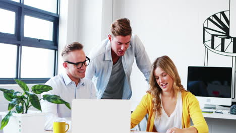 Businesswoman-interacting-with-coworkers-while-working-on-laptop