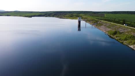 Flying-over-abandoned-dam-with-reflecting-sky-on-water