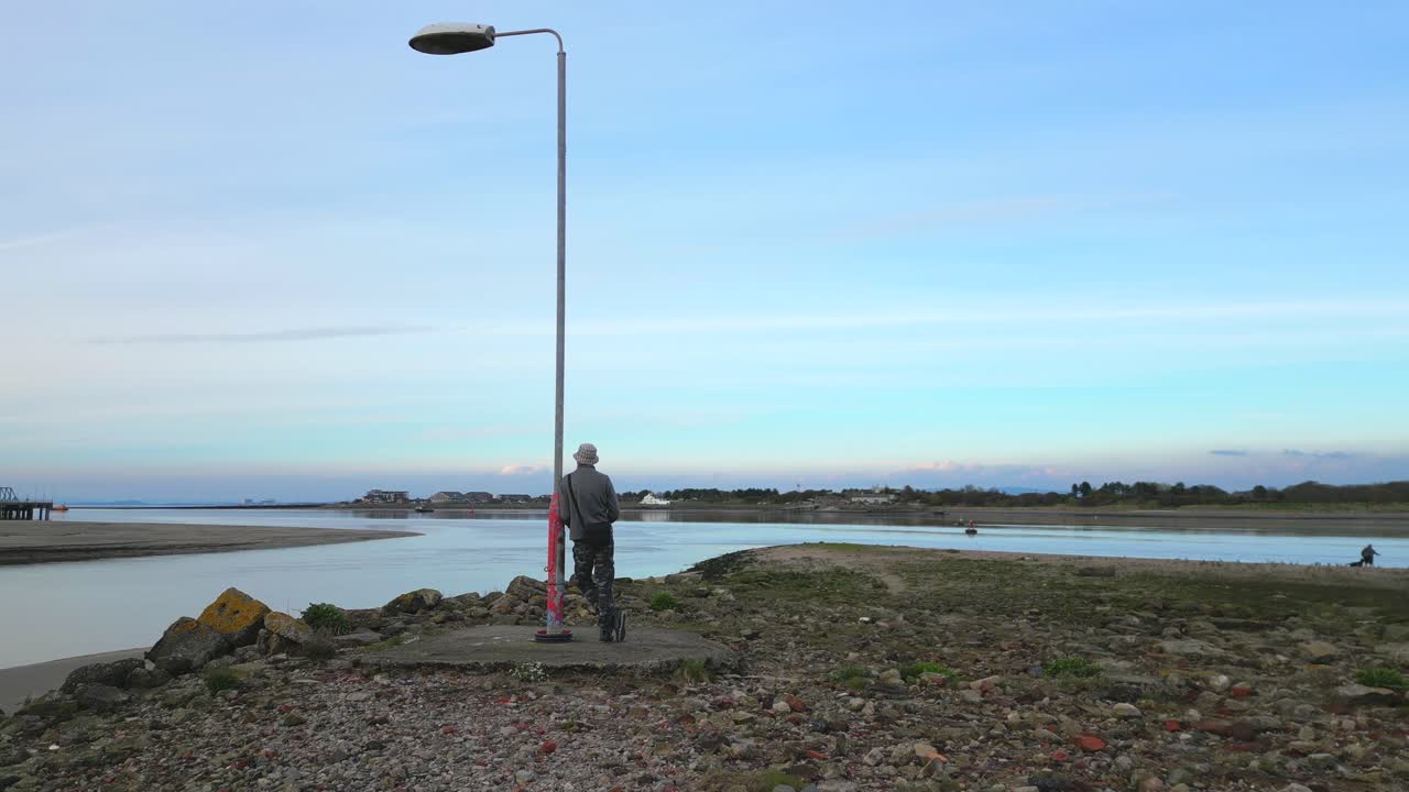 Man leaning against solitary lamppost on waste ground at the River Wyre estuary Fleetwood Lancashire UK