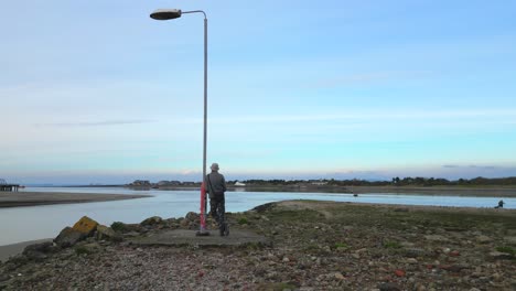 Mann-Lehnt-An-Einem-Einsamen-Laternenpfahl-Auf-Brachland-An-Der-Mündung-Des-Flusses-Wyre,-Fleetwood,-Lancashire,-Großbritannien