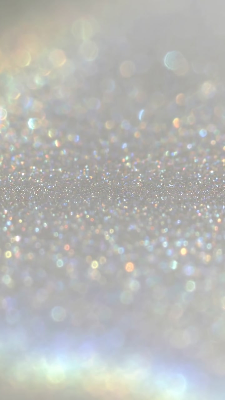 Vertical video: Shifting light and focus causing shiny glitter shining in studio bokeh rainbow band