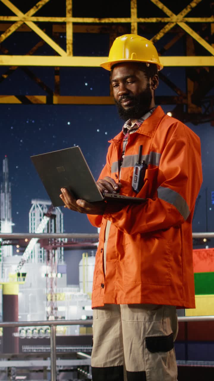 Vertical Video Black offshore engineer monitoring oil rig platform operation using laptop