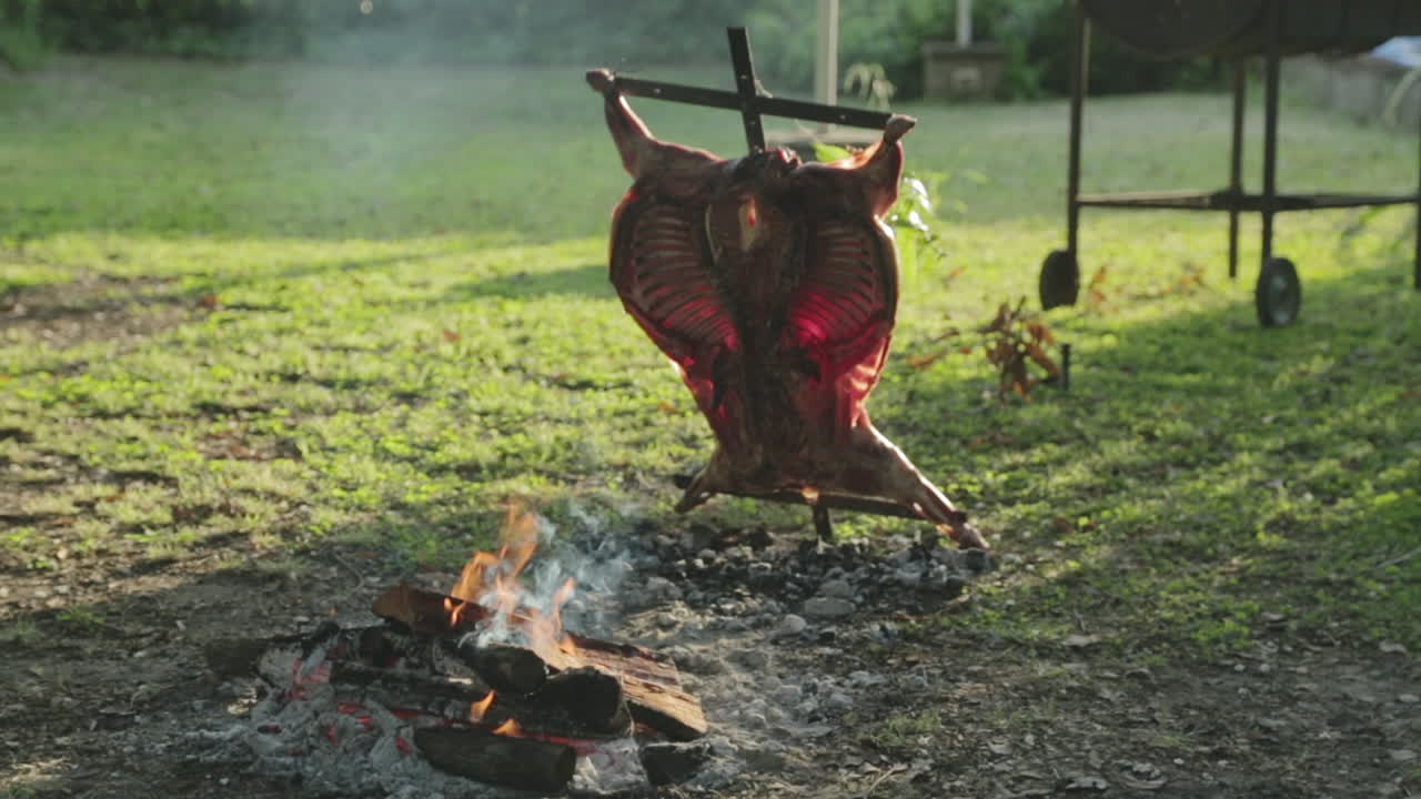 el fuego está ardiendo junto a la carne de cordero siendo cocinada y asada en una cruz de metal asado