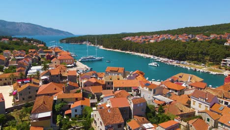 vista de un pueblo costero con muchas casas con techos rojos, rodeado por el mar y las montañas con yates en marina bay y campanario