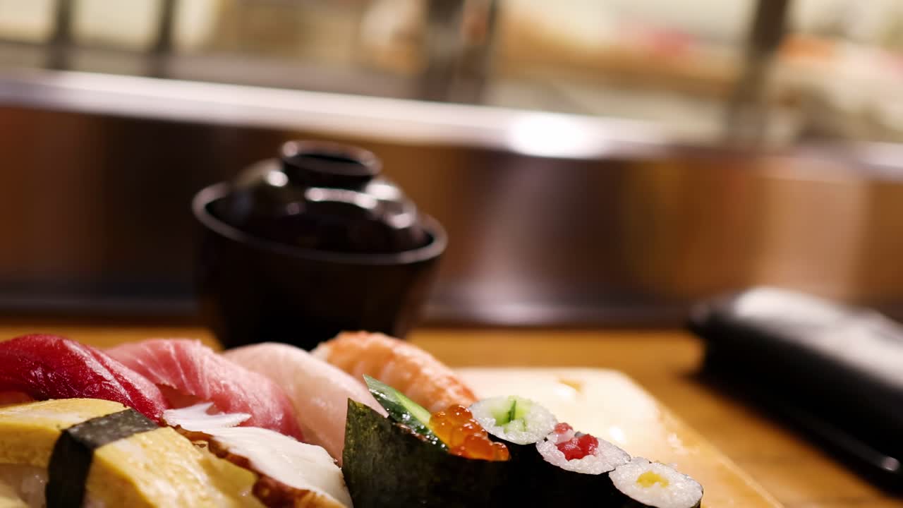 A detailed view of assorted sushi pieces with a soy sauce container on a wooden board.